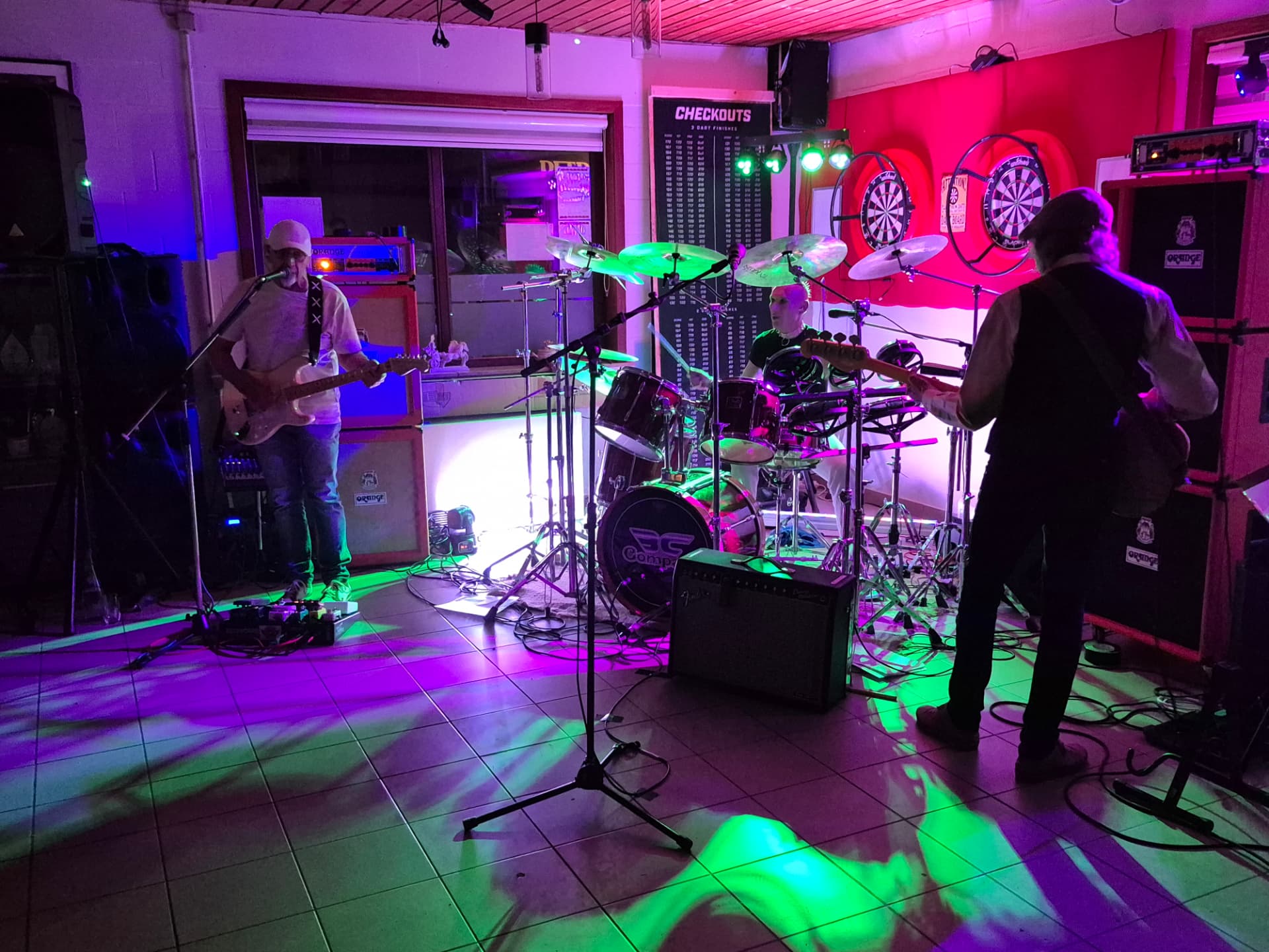 Liveband speelt in het café tussen de dartborden door, met gekleurde lichten