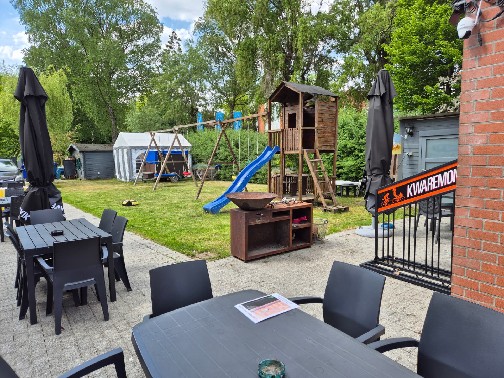 Terras met tafels en zicht op de speeltoren, glijbaan en schommels in de tuin