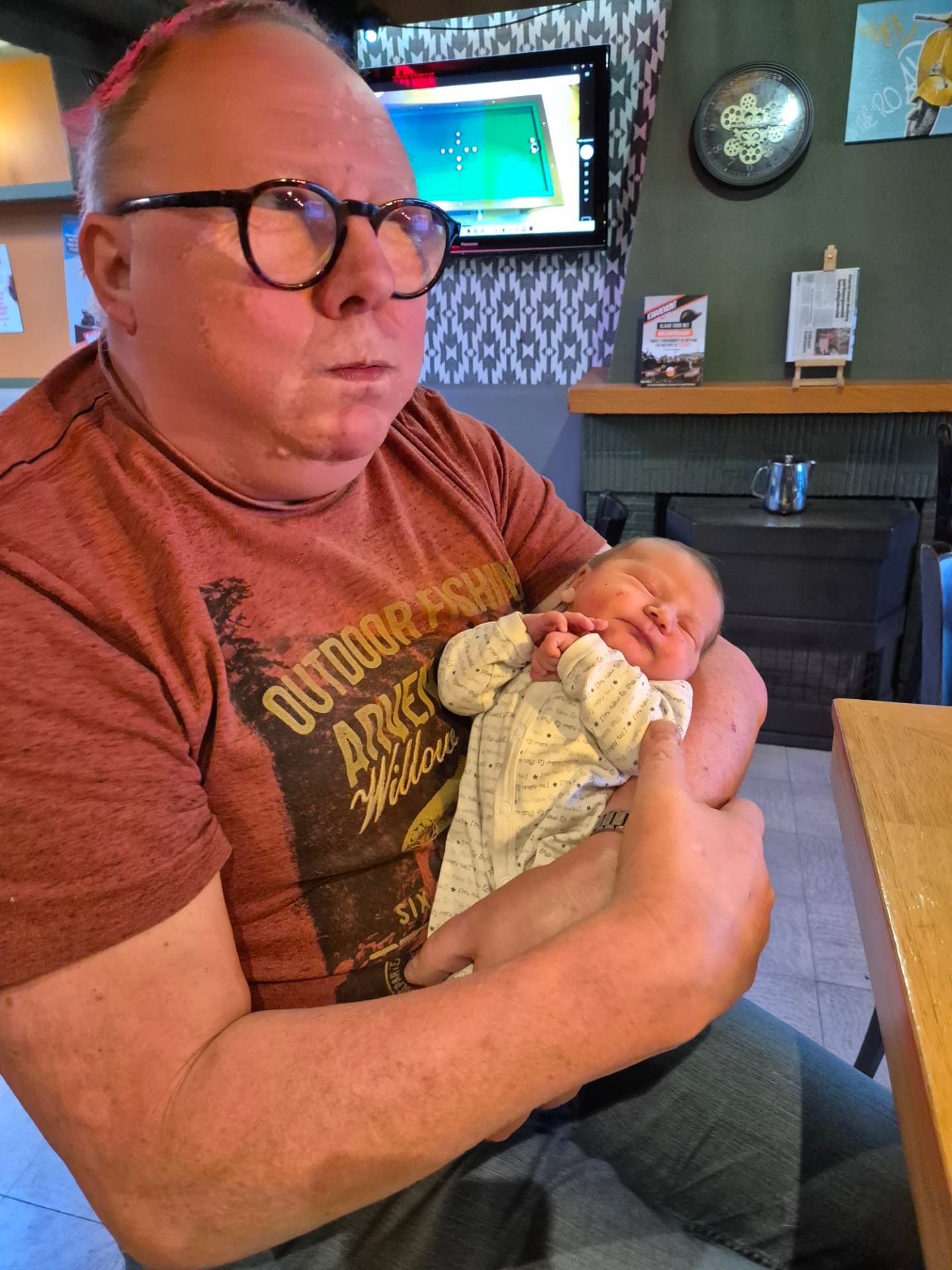 Een pasgeboren baby slaapt in de armen van een vaste gast in het café